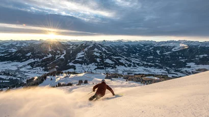 Skifahrer fährt bei Sonnenuntergang einen schneebedeckten Berg hinunter