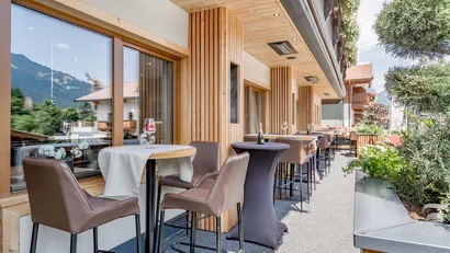 Außenbereich mit Bistrotischen, Stühlen und Holzakzenten an einem Gebäude