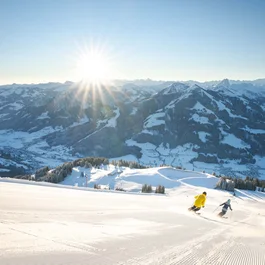 Zwei Skifahrer auf verschneiter Piste bei strahlendem Sonnenschein in den Bergen