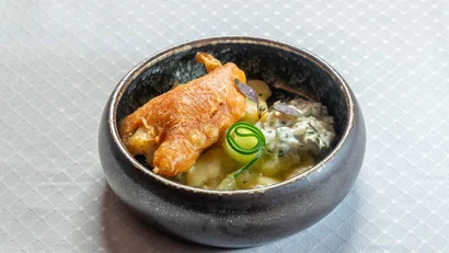 Frittierter Fisch mit Kartoffelsalat in schwarzer Schale auf weißer Tischdecke