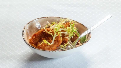 Schüssel mit paniertem Schnitzel und Salatblättern, Gabel darin