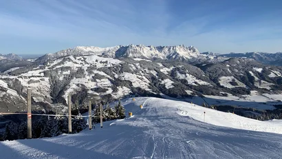 Schneebedeckte Skipiste mit Bergen im Hintergrund unter klarem blauen Himmel