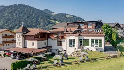 Hotelgebäude in den Bergen mit Liegestühlen und Sonnenschirmen im Garten