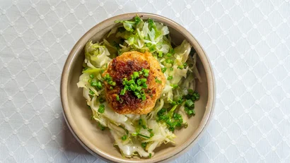 Bratling auf Salat mit Frühlingszwiebeln in beigem Ovalteller