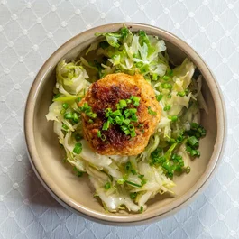 Fried patty on salad with chopped spring onions in beige oval dish