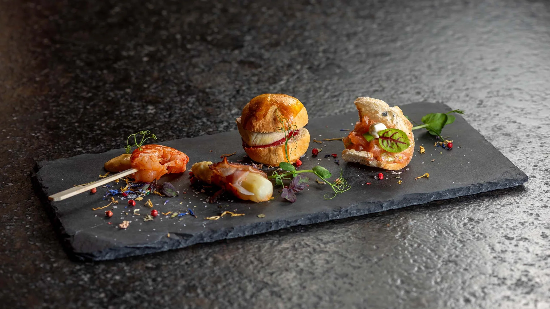 Verschiedene Appetithäppchen auf einer schwarzen Schieferplatte angerichtet